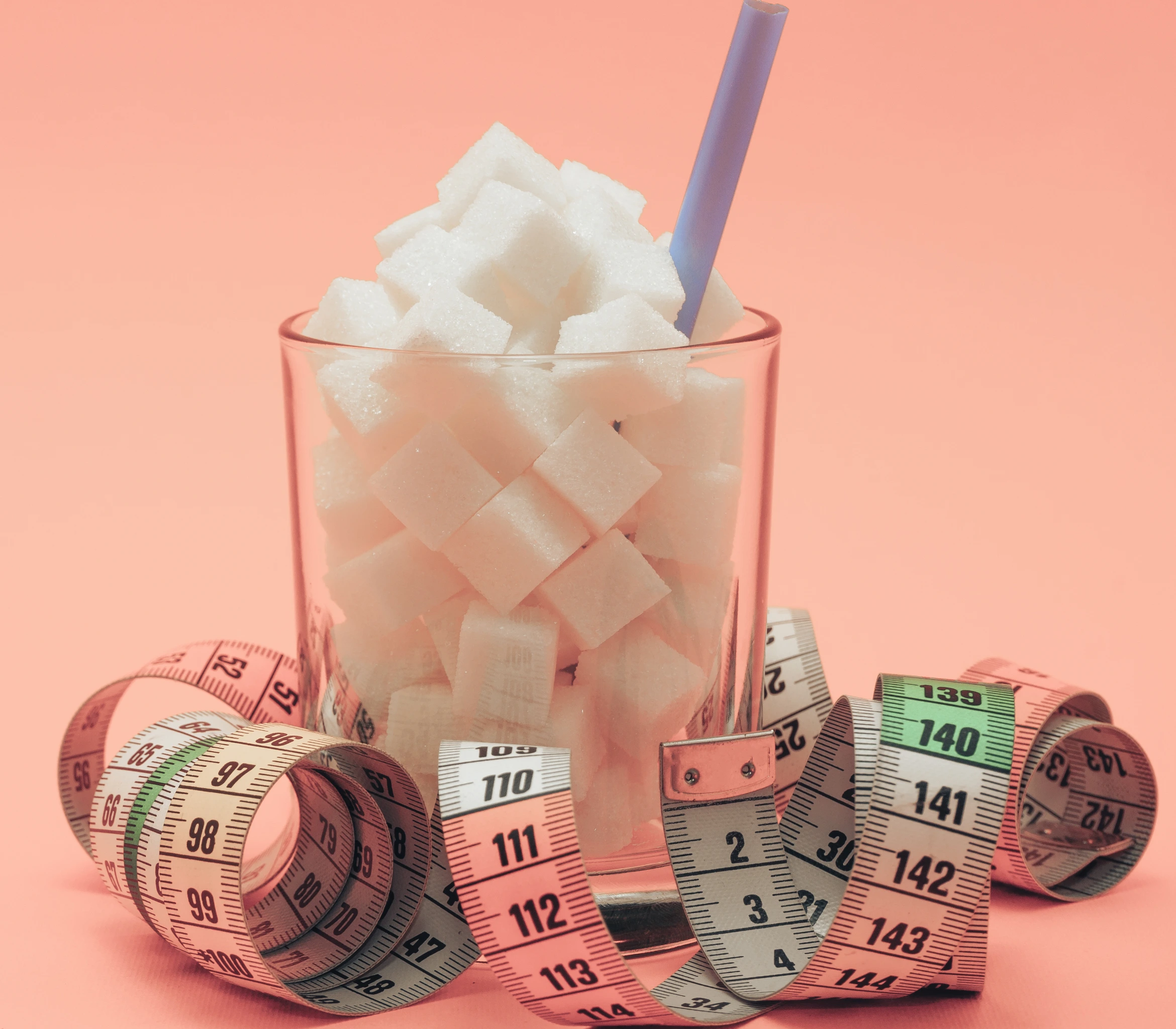 Glass full of cubes sugar with straw on a beautiful peach  background  - unhealthy diet concept.