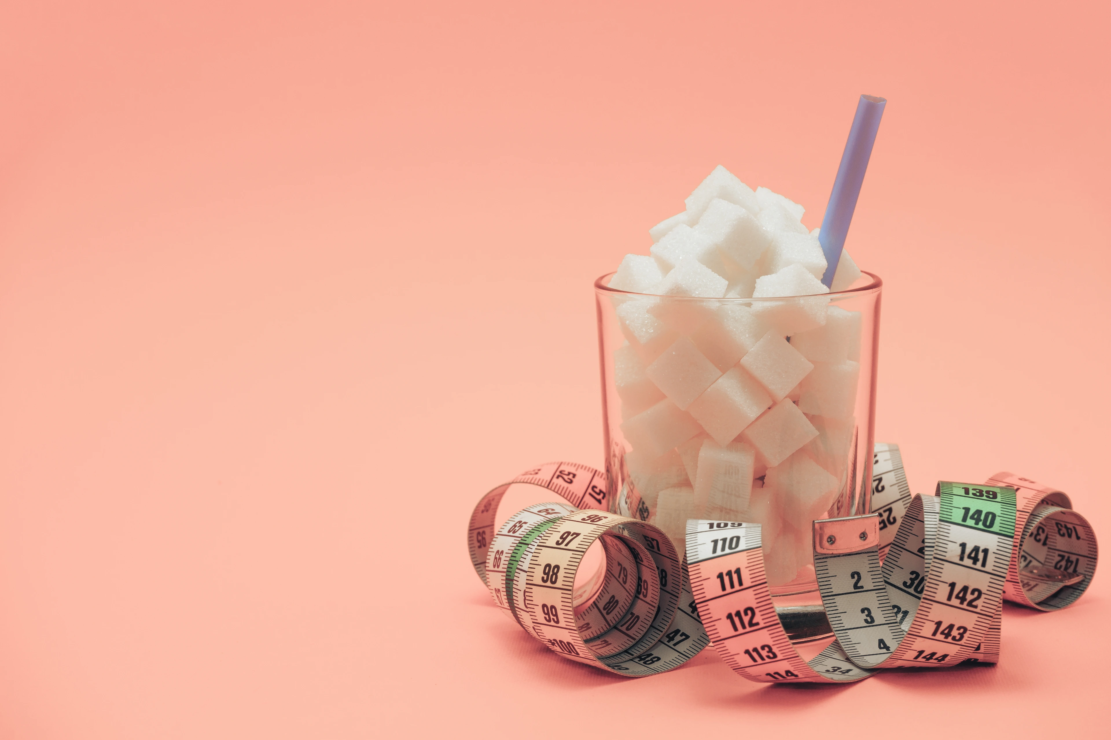 Glass full of cubes sugar with straw on a beautiful peach  background  - unhealthy diet concept.