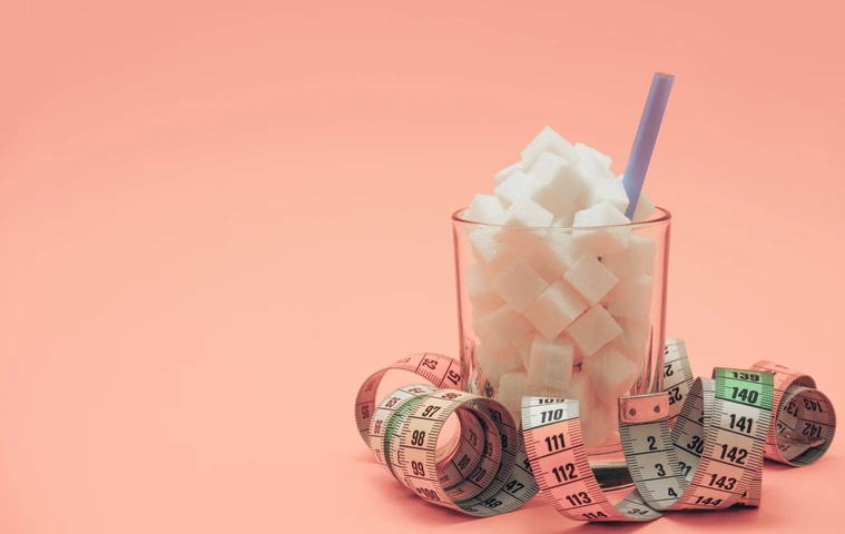 Glass full of cubes sugar with straw on a beautiful peach  background  - unhealthy diet concept.