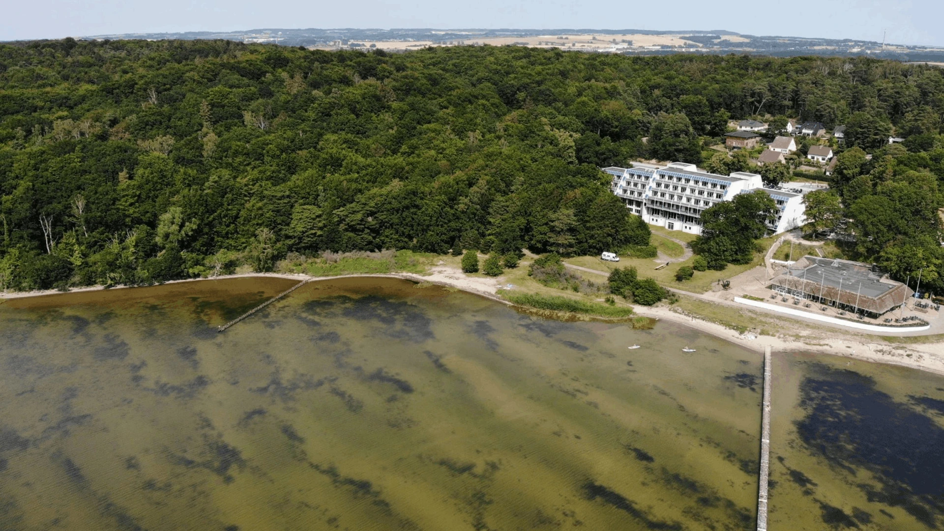 Luftaufnahme eines Waldes an der Küste mit Strand, Steg und einem Hotel von PALMBERG