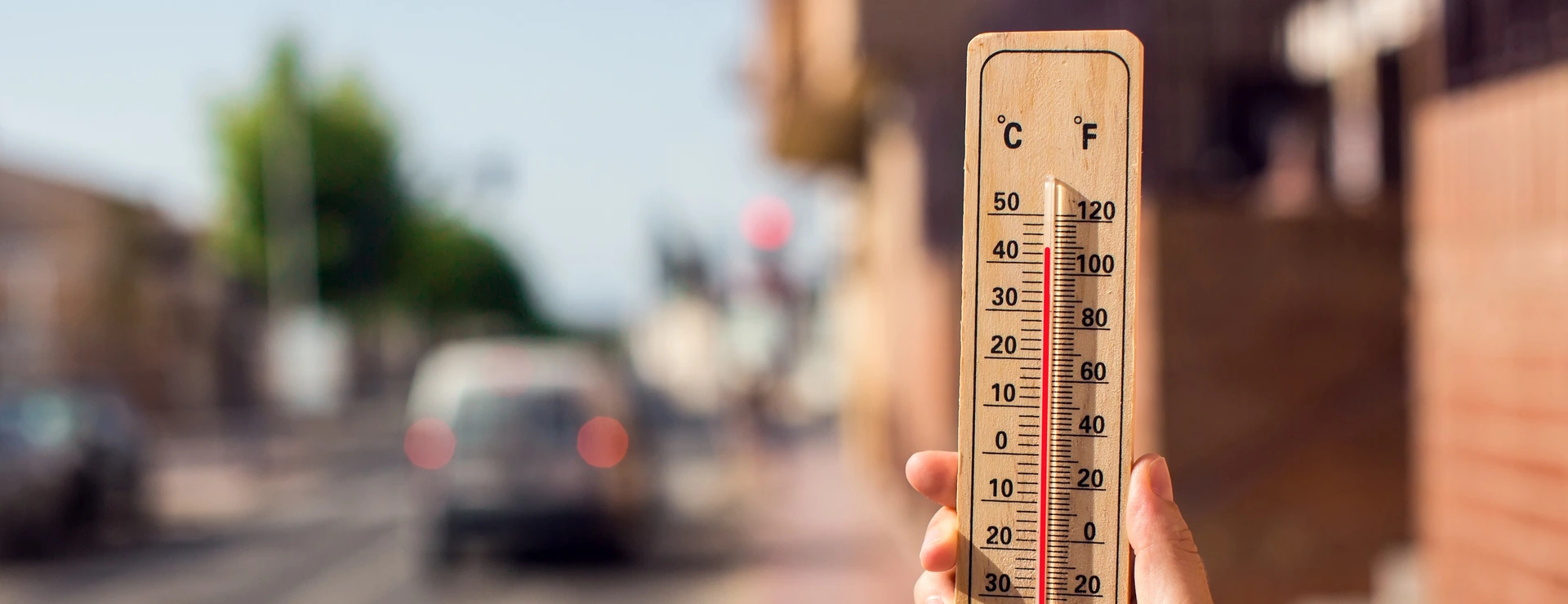 Hot weather. Thermometer in front of an urban scene during heatwave.