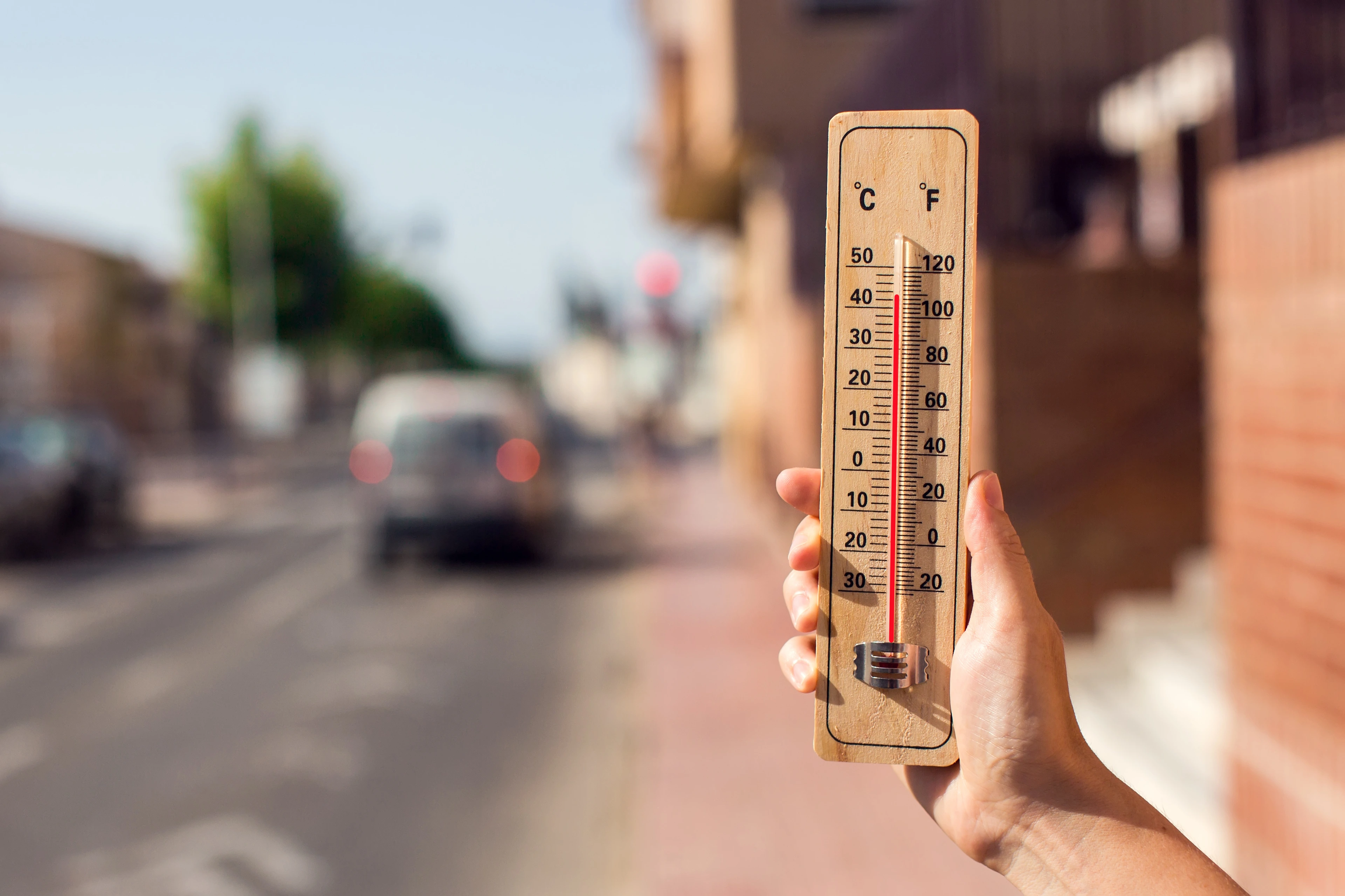 Hot weather. Thermometer in front of an urban scene during heatwave.