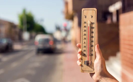 Hot weather. Thermometer in front of an urban scene during heatwave.