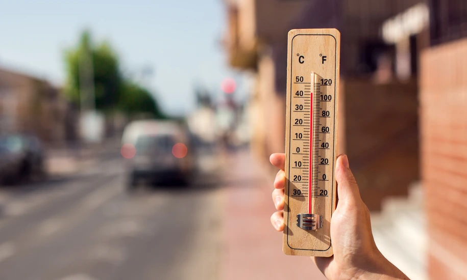 Hot weather. Thermometer in front of an urban scene during heatwave.
