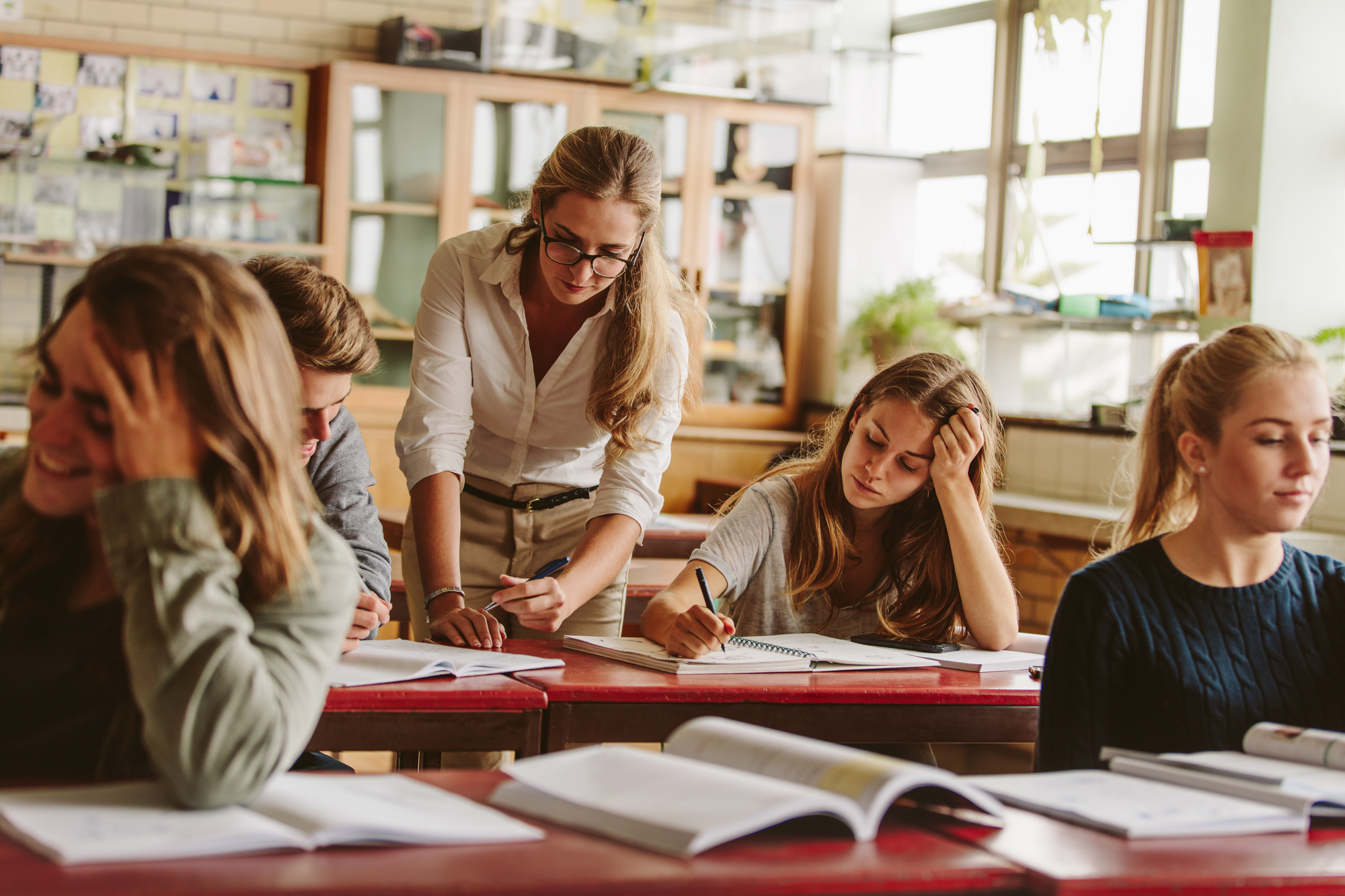 Lehrerin unterstützt mehrere Schüler*innen bei der Arbeit an Aufgaben im Klassenzimmer