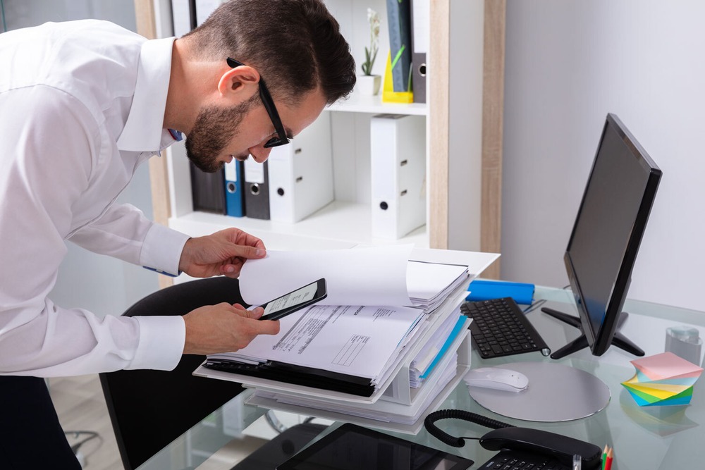 Ein Mann in Business-Kleidung fotografiert mit seinem Smartphone Unterlagen aus einem Aktenordner