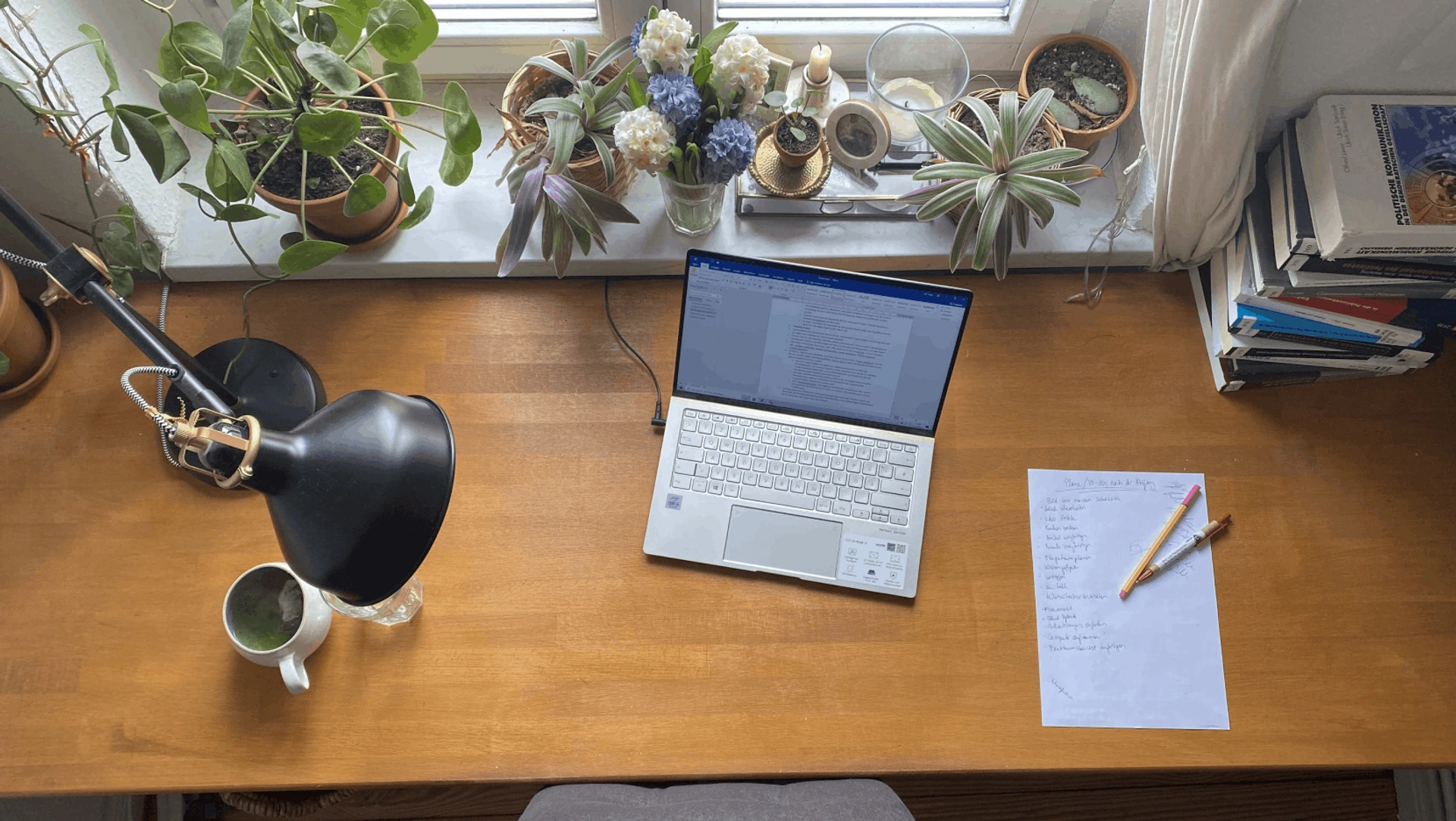 PALMBERG-Schreibtisch mit offenem Laptop, Lampe, Kaffeetasse, Pflanzen und handschriftlicher Liste