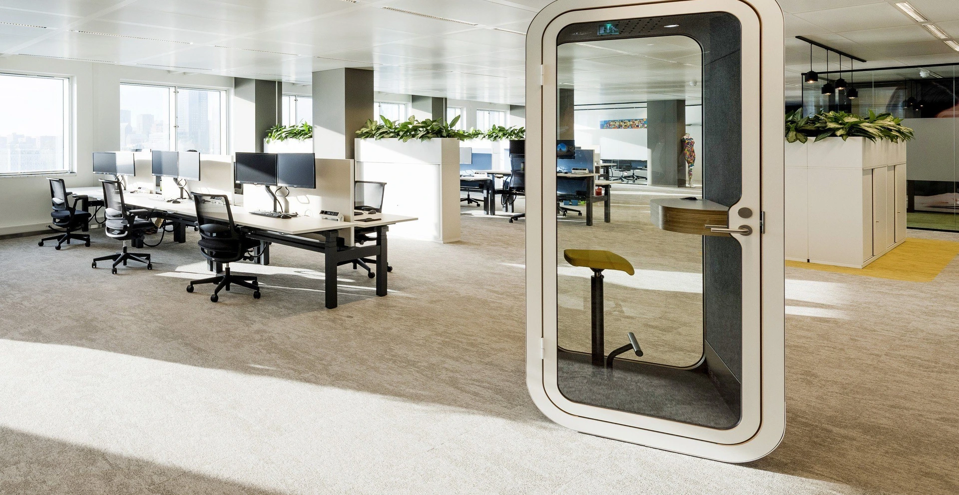 Helles offenes Büro mit Tischen, Pflanzen und einer PALMBERG-Telefonkabine mit Hocker.
