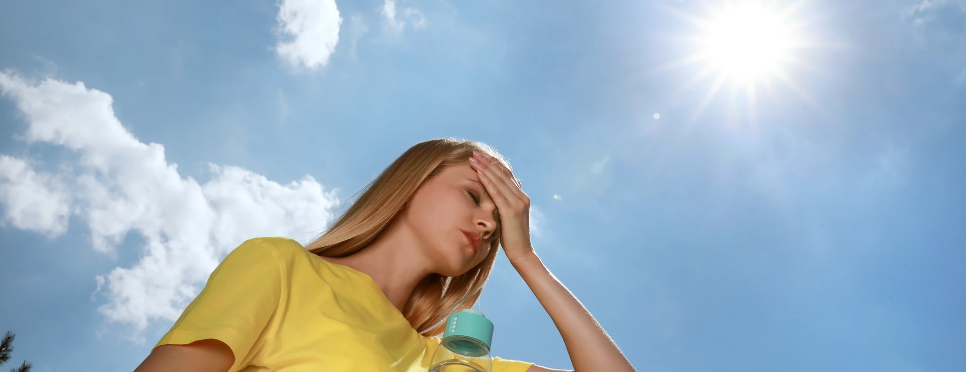 Woman with bottle of water suffering from heat stroke outdoors