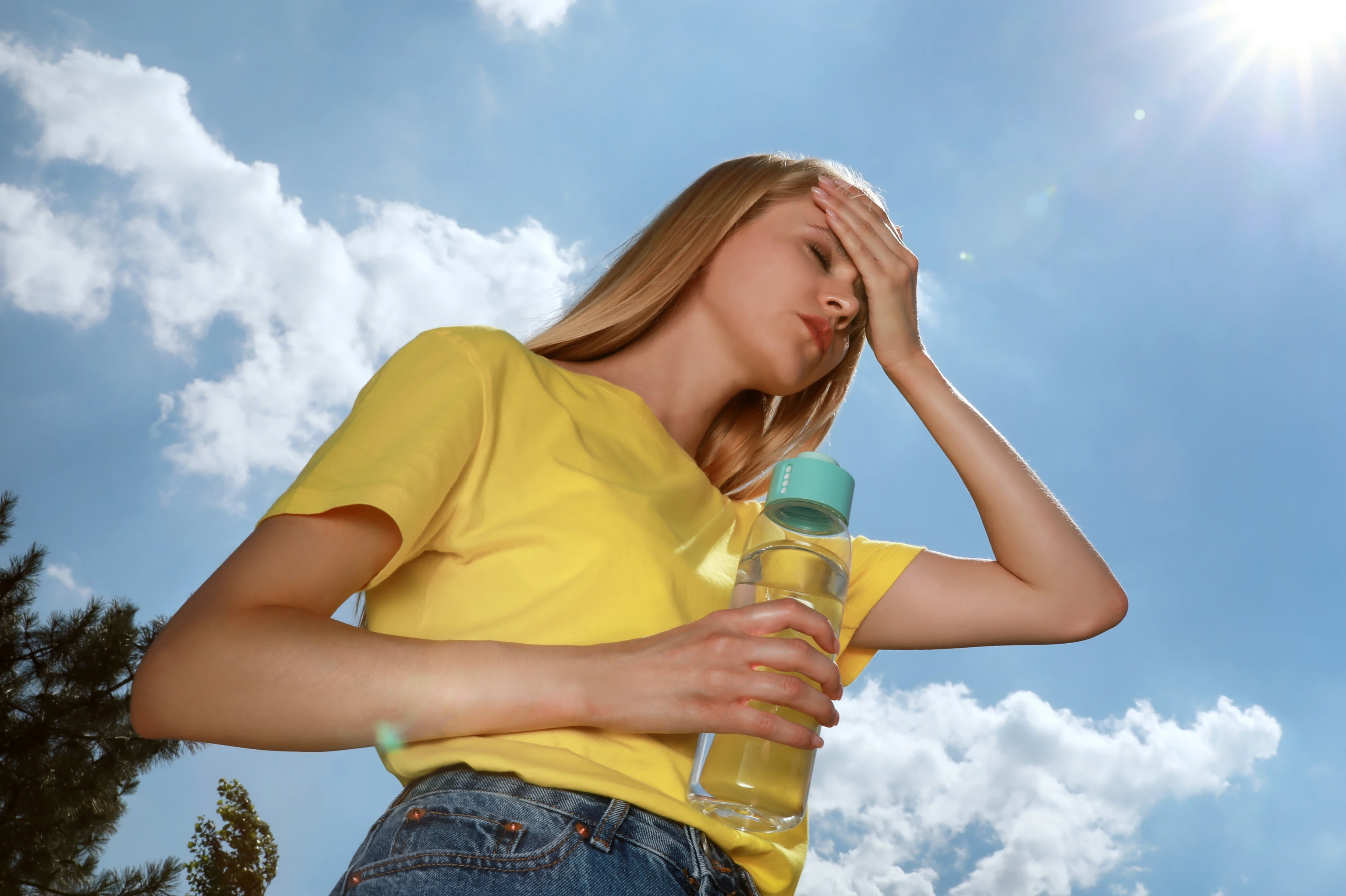 Woman with bottle of water suffering from heat stroke outdoors