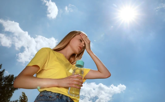 Woman with bottle of water suffering from heat stroke outdoors