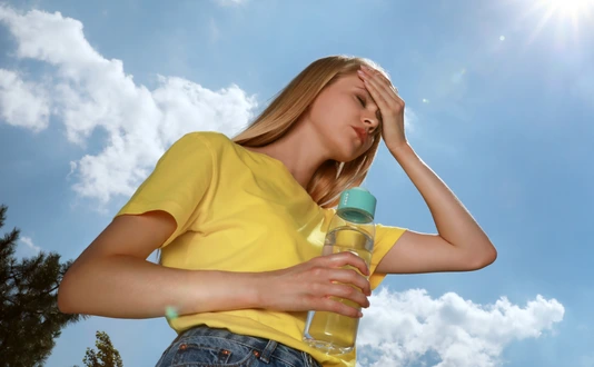 Woman with bottle of water suffering from heat stroke outdoors