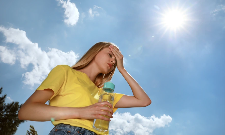 Woman with bottle of water suffering from heat stroke outdoors