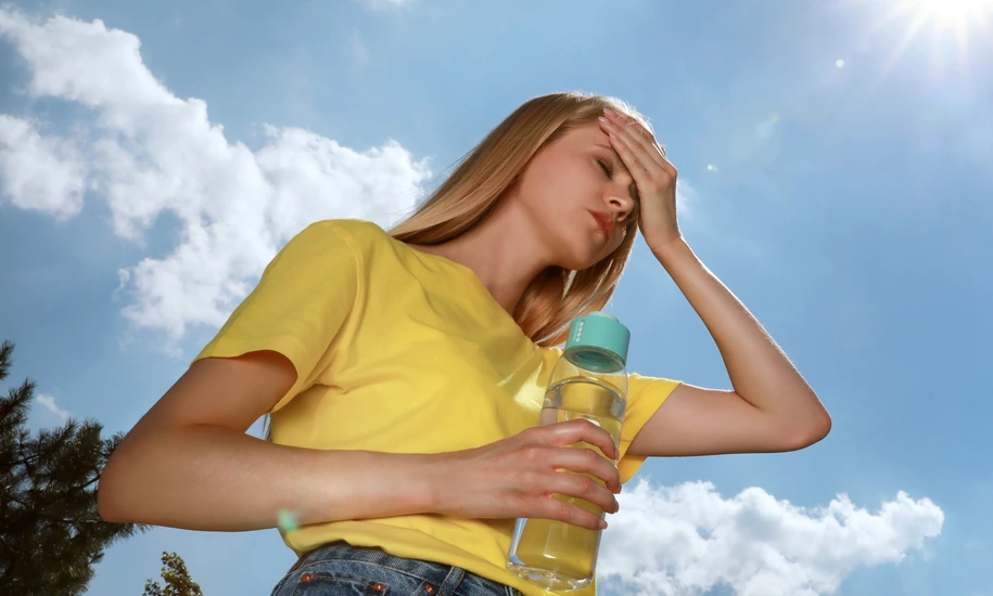 Woman with bottle of water suffering from heat stroke outdoors