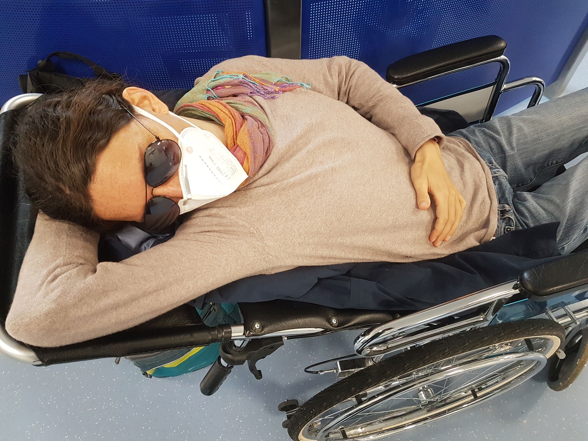 Krankheit ME/CFS betroffene Frau mit Mundschutz und Sonnenbrille kraftlos in Rollstuhl