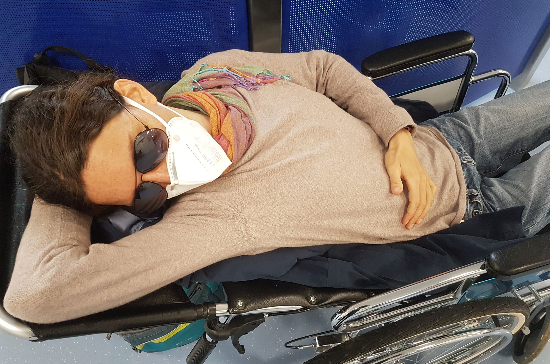 Krankheit ME/CFS betroffene Frau mit Mundschutz und Sonnenbrille kraftlos in Rollstuhl