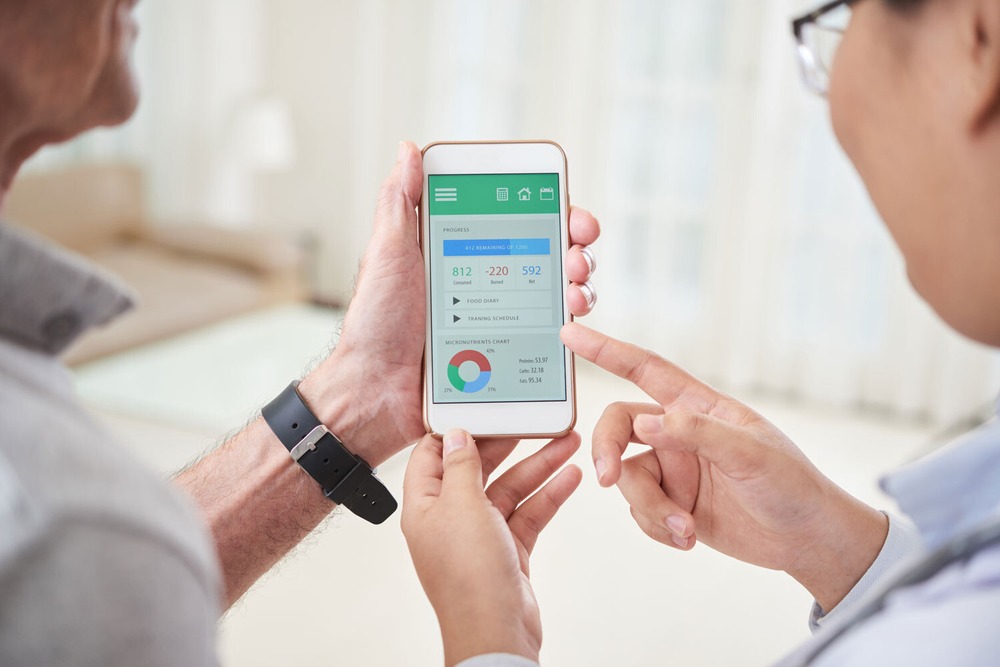 Ein Smartphone, auf dem eine digitale Gesundheitsanwendung zu sehen ist, zwei Personen, eine hält Smartphone in der Hand, beide betrachten den Bildschirm